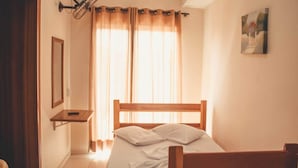A bedroom with a wooden bed, a nightstand, a wall-mounted fan, and a window with curtains. - Hotel Piracicaba (Aparecida)