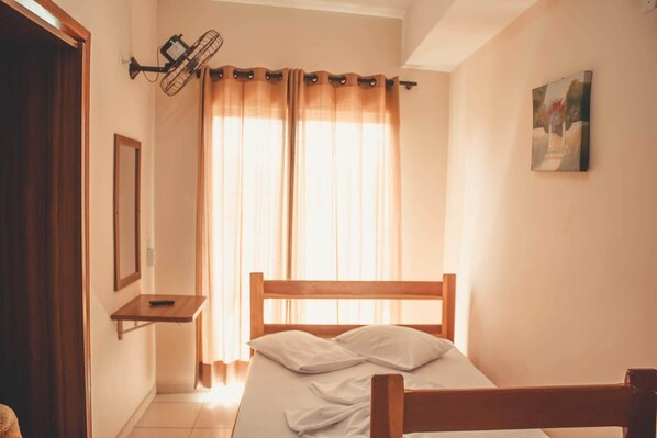 A bedroom with a wooden bed, a nightstand, a wall-mounted fan, and a window with curtains.