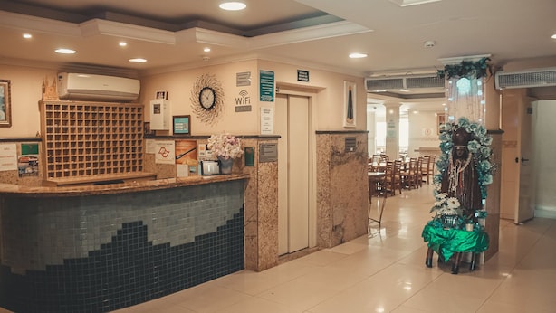 A hotel reception area with a tiled counter, a clock, WiFi sign, and a decorative plant. - Hotel Piracicaba (Aparecida)