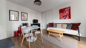 Una sala de estar moderna con una mesa de comedor redonda, un sofá con cojines rojos y grises, un televisor y obras de arte en las paredes.