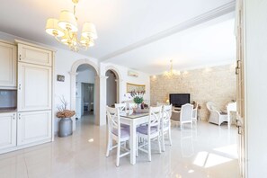 A spacious dining area with white furniture, a stone wall, and a chandelier.