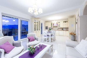A modern living room with a dining area, a kitchen, and a large sliding glass door leading to a balcony with a city view.