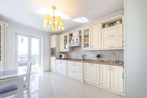 A modern kitchen with white cabinetry, a built-in oven, a microwave, and a large window.