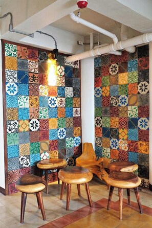 A room with a colorful patchwork wall, wooden stools, and a hanging light fixture. - Saeng Panya Home - Boutique Residence (Chiang Mai)
