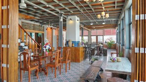 A spacious room with a high ceiling, wooden beams, a central dining table with chairs, a bar area, and large windows. - Saeng Panya Home - Boutique Residence (Chiang Mai)