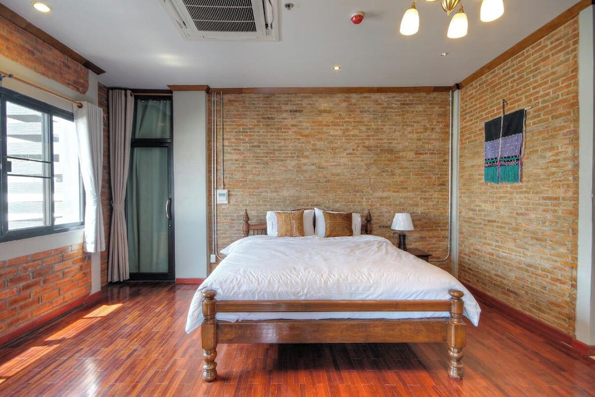 Ein Schlafzimmer mit einem hölzernen Bett, Ziegelwänden, einem Fenster und einer Tür.