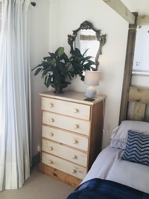 Cozy retreat with a dresser, potted plant, and reading lamp, featuring a comfortable bed with a stylish headboard.