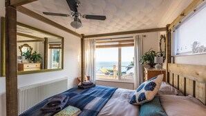 A bedroom with a bed, a ceiling fan, a window with a view, a dresser, and a mirror. - 1 Bed Flat - Sleeps 2 - Pets - Balcony - Parking (Looe)