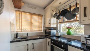 A kitchen with white cabinets, a black countertop, a stove, an oven, and a window with blinds. - 1 Bed Flat - Sleeps 2 - Pets - Balcony - Parking (Looe)