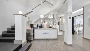 Un hall d’hôtel moderne comprenant un comptoir d’accueil, un escalier et un espace repas.
