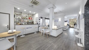 Un espace bar moderne, avec des meubles blancs, une machine à café et une variété de bouteilles exposées sur des étagères.