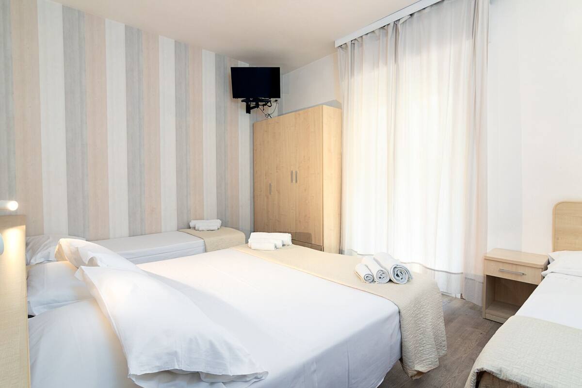 Habitación de hotel con dos camas, un armario de madera, un televisor y una mesita de noche con teléfono.