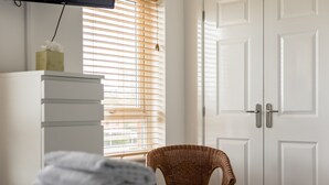 Une pièce avec une armoire blanche, une chaise en osier et un lit recouvert d’une couverture blanche.