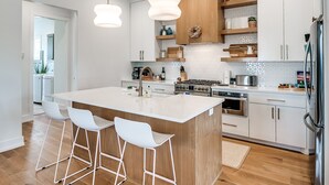 Una cocina moderna con armarios blancos, una isla de madera, taburetes de bar y electrodomésticos de acero inoxidable.