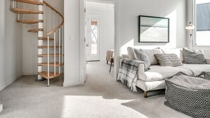 Una sala de estar moderna con una escalera espiral, un juego de sofás y un gran ventanal que proporciona luz natural.