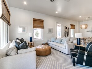 Relax in this stylish living room with a sofa, armchair, and dining area, offering a view of the outdoors through a large window.