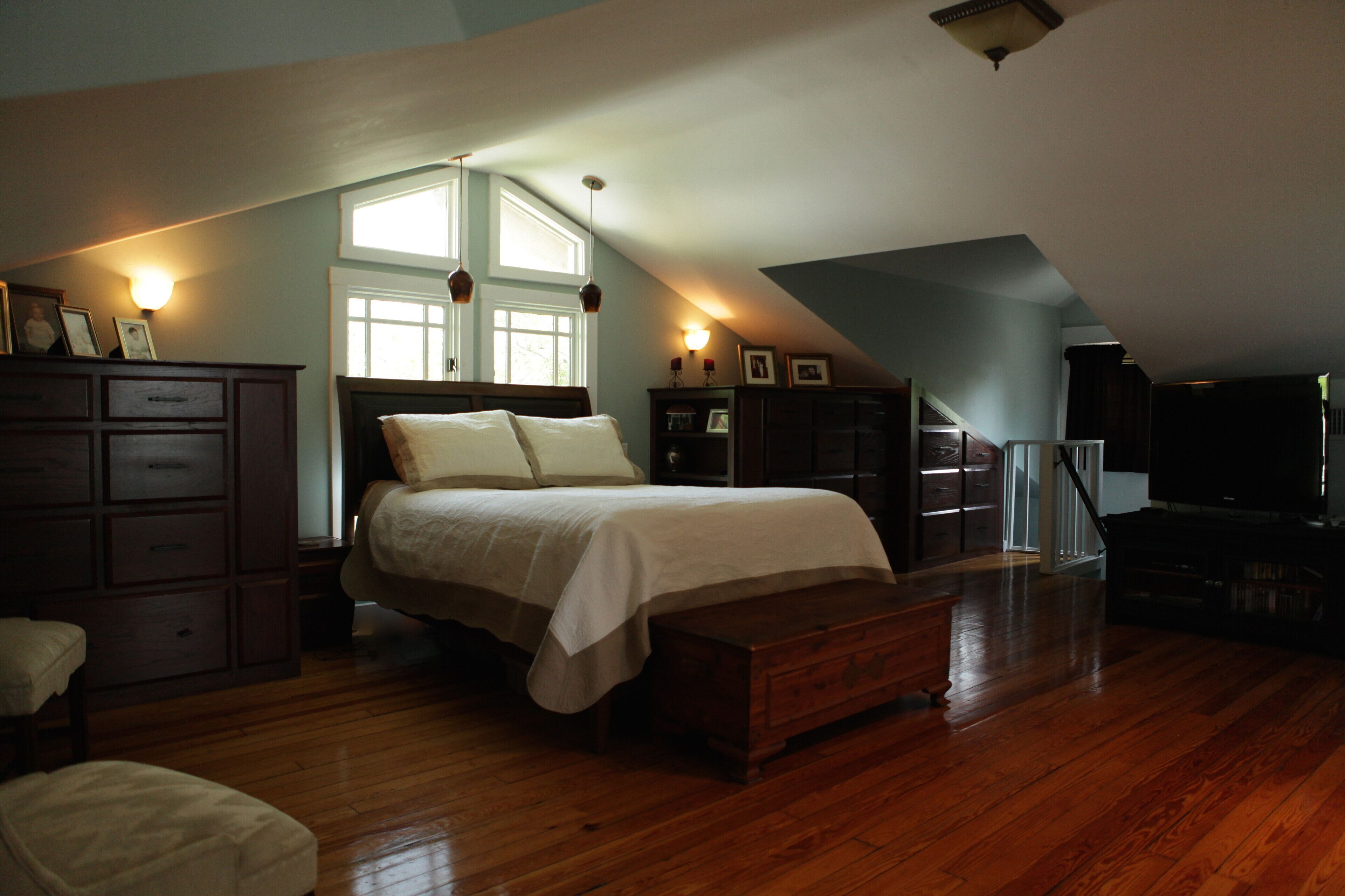 Een slaapkamer met een groot bed, houten vloer, een dressoir, een bankje en een televisie.