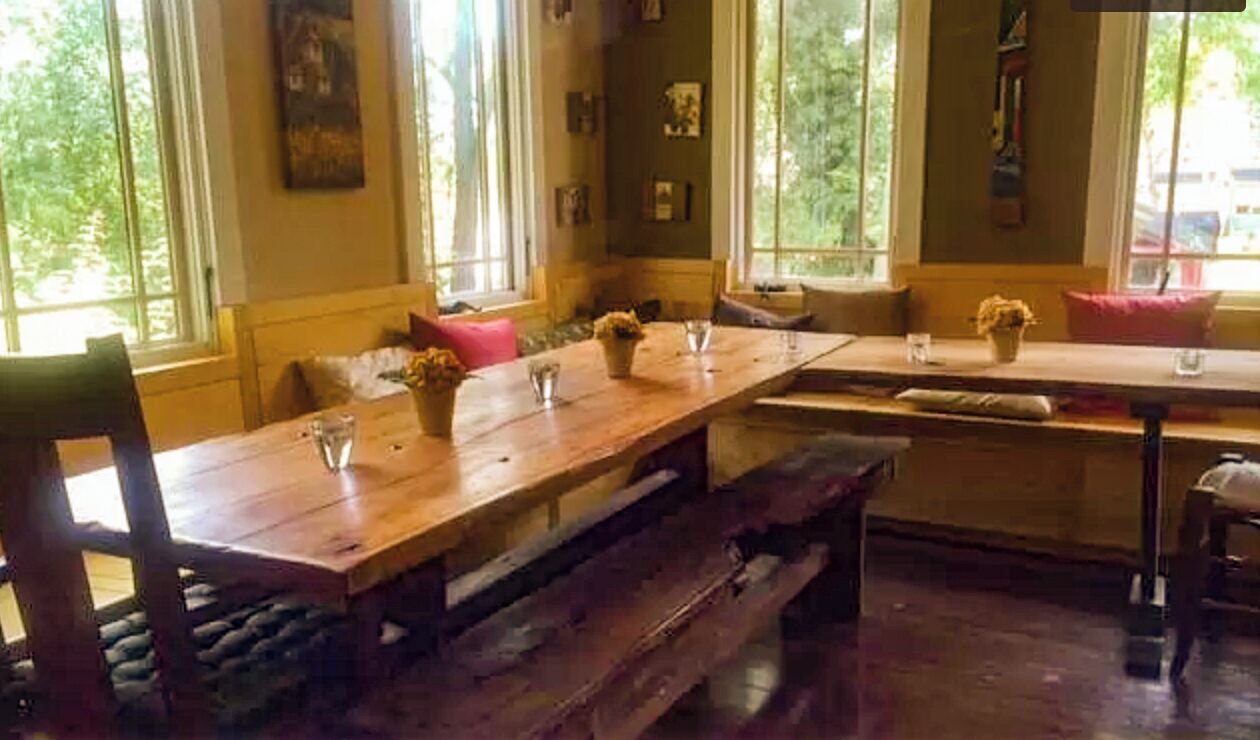 Een eetruimte met een houten tafel, bankjes en stoelen. Er zijn ramen met uitzicht op groen.