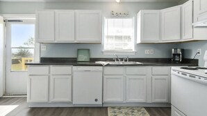 A kitchen with white cabinets, a built-in dishwasher, a stove, and a window with blinds. - 2 Beach view Cottages, Perfect family get together (Gulfport)