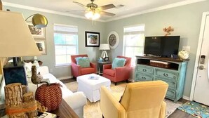 A living room with a ceiling fan, a television, and two red armchairs. - 2 Beach view Cottages, Perfect family get together (Gulfport)