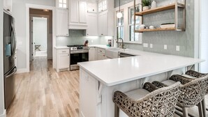 Una cocina moderna con armarios blancos, una isla grande y sillas de mimbre.