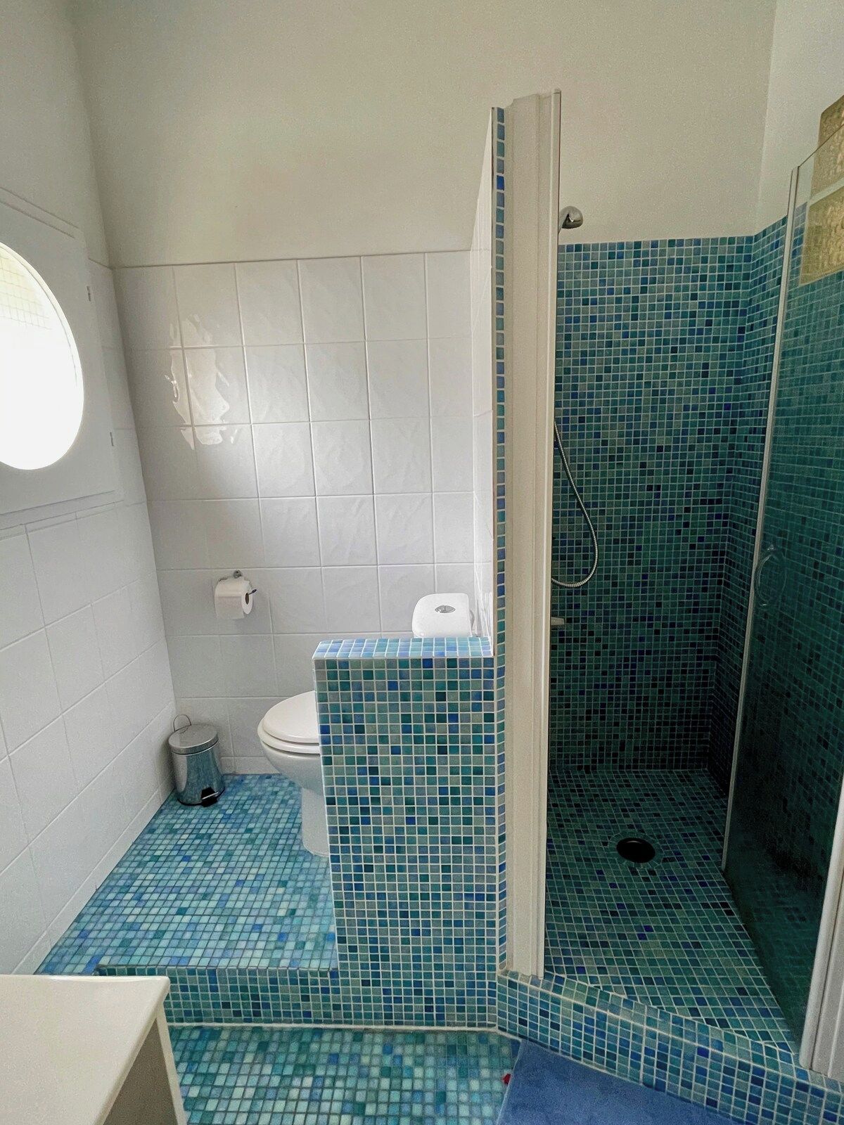 Ein Badezimmer mit einer weißen Toilette, einem blauen Fliesen-Duschbereich und einem weißen Waschbecken.