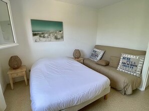 A bedroom with a large bed, a sofa, a small table, and a wall-mounted lamp.
