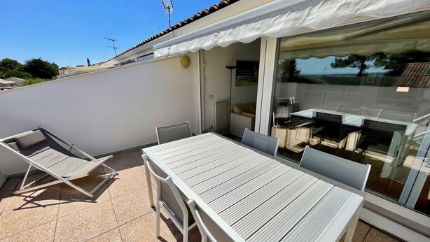 Un patio con mesa y sillas, una puerta corrediza de vidrio y un toldo blanco.