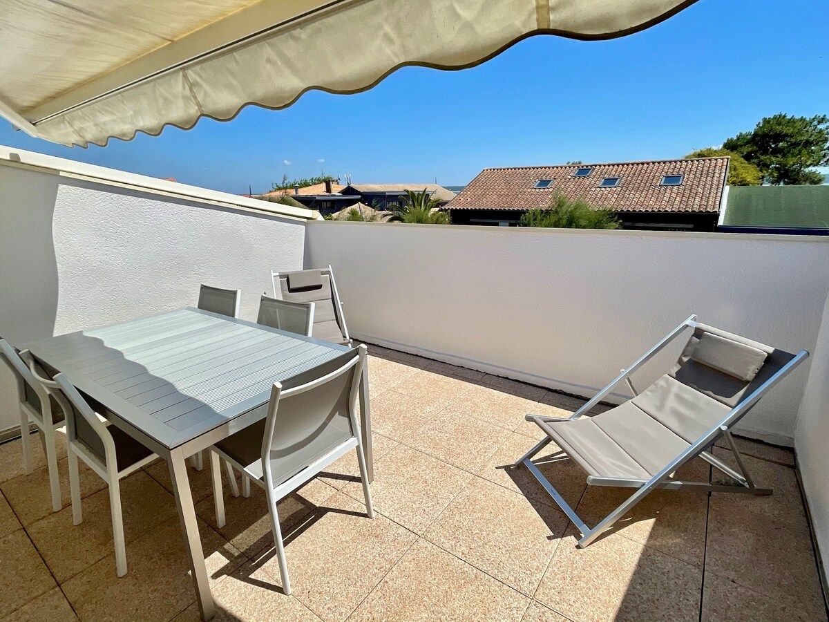 Un patio exterior con una mesa, sillas, una tumbona y una pared blanca.