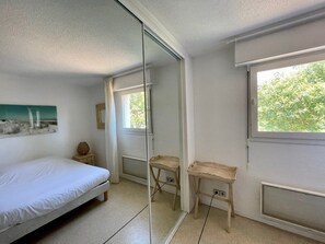 A bedroom with a bed, a small table, a mirror, and a window. - Lovely apartment with terrace in Cap Ferret A0312 (Lège-Cap-Ferret)