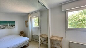 Un dormitorio con cama, mesita de noche, espejo y ventana con vistas a árboles.