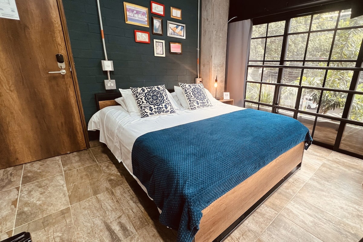 Un dormitorio moderno con una cama grande, vistas a la vegetación por una ventana y una puerta de madera.