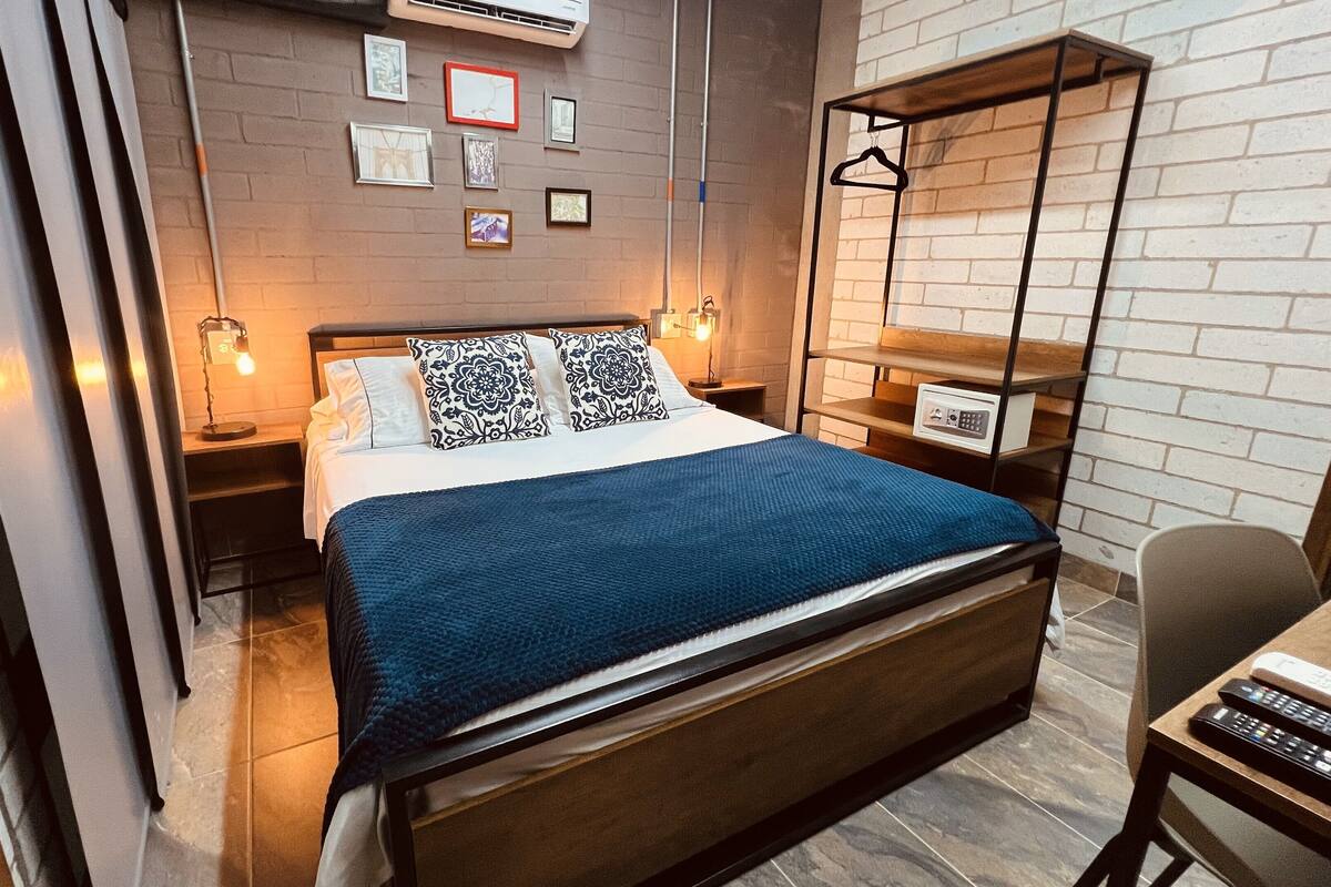 Un dormitorio moderno con una cama grande, una mesita de noche con lámpara, un armario y una percha.