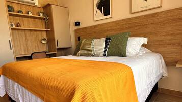 Une chambre d’hôtel moderne avec un grand lit, une tête de lit en bois et un plaid jaune vif.