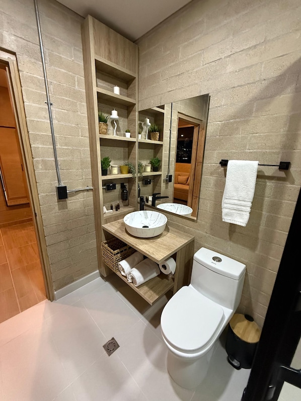 A modern bathroom with a wooden vanity, a large mirror, a white sink, and a toilet. - Manila Hotel Boutique (Medellín)