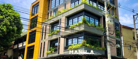 A multi-story hotel with a modern design, featuring balconies with greenery, a visible entrance, and a sign indicating it is a hotel.