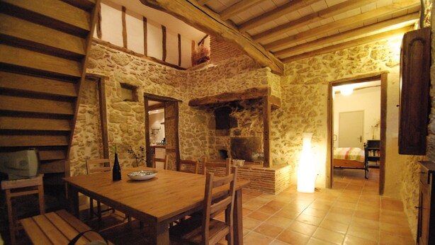 Un interior rústico de piedra con una mesa de comedor de madera, bancos y una chimenea de piedra.