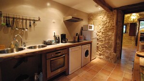 Una cocina con pared de piedra, vigas de madera, lavadora y microondas.