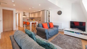 Una sala de estar moderna con un sofá, televisión y una cocina al fondo.