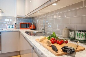 A modern kitchen with a built-in microwave, stainless steel sink, and a cutting board with tomatoes and cheese.