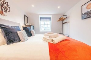 A bedroom with a bed, pillows, a window, a nightstand, and a towel rack.