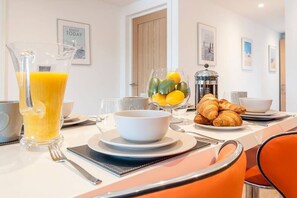 A breakfast setting with a pitcher of orange juice, a bowl of fruit, croissants, and a coffee machine. - Magnificent views of Tamar and Rwy. Free Parking (Plymouth)