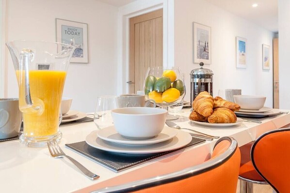 A breakfast setting with a pitcher of orange juice, a bowl of fruit, croissants, and a coffee machine.