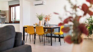 A modern dining area with a table and chairs, a vase with flowers, and an air conditioning unit on the wall. - Villa Etesiae (Castellammare del Golfo)