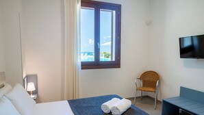 A hotel room with a bed, a chair, a TV, and a window with a view of a pool. - Villa Etesiae (Castellammare del Golfo)