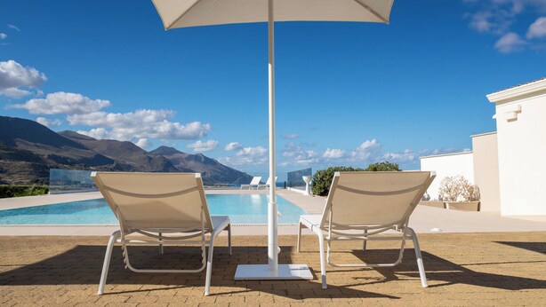 A poolside area with two lounge chairs and a large umbrella, overlooking a mountain range. - Villa Etesiae (Castellammare del Golfo)