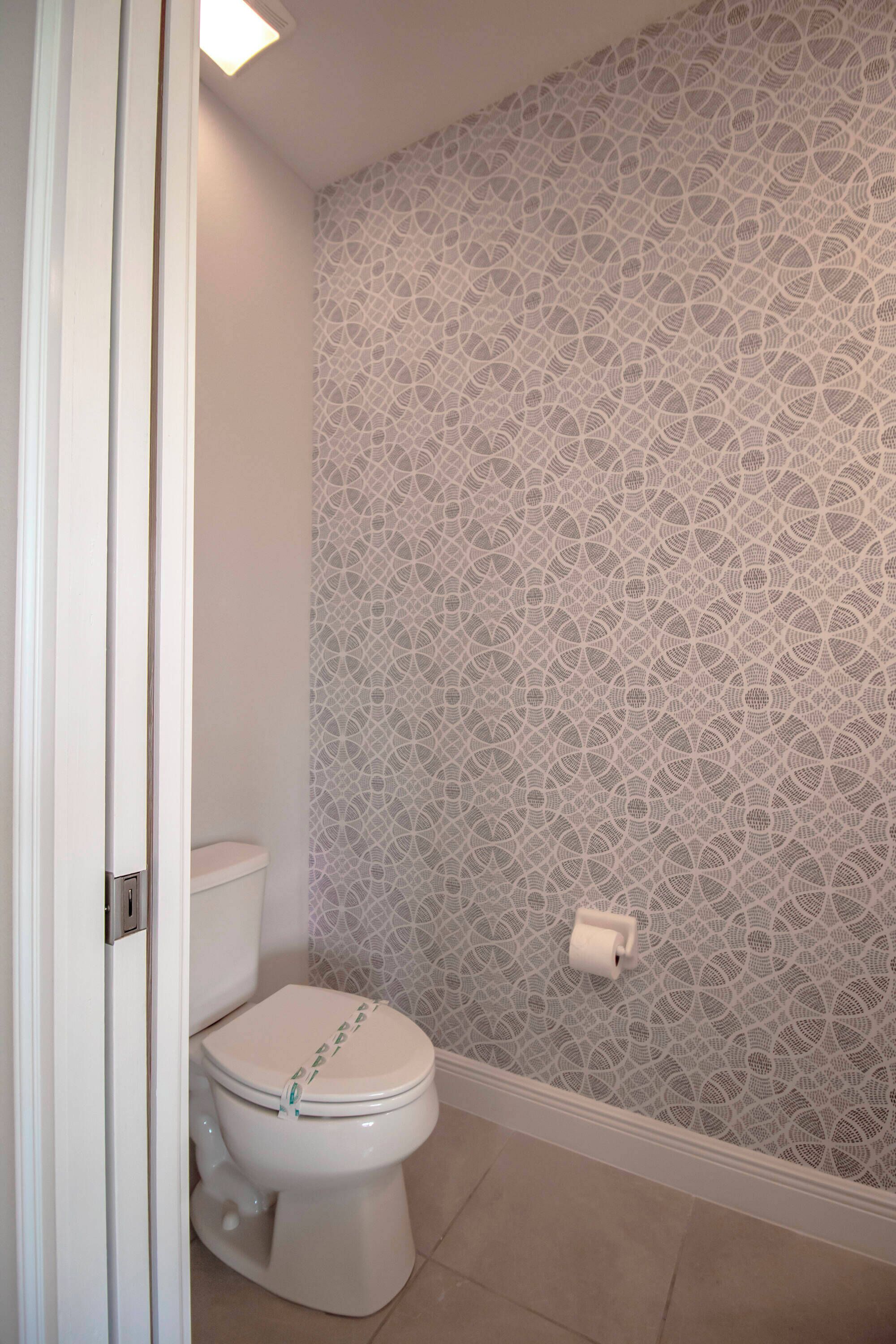 A bathroom with a toilet, patterned wallpaper, and a roll of toilet paper on the wall.
