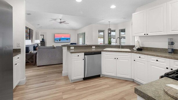 A modern kitchen with white cabinets, a dishwasher, and a grey countertop.