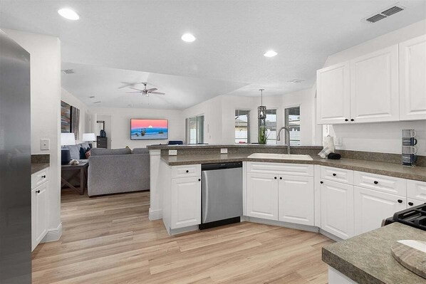 A modern kitchen with white cabinets, a dishwasher, and a grey countertop.