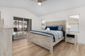 A bedroom with a wooden bed, a nightstand, a ceiling fan, and a view of an outdoor patio.